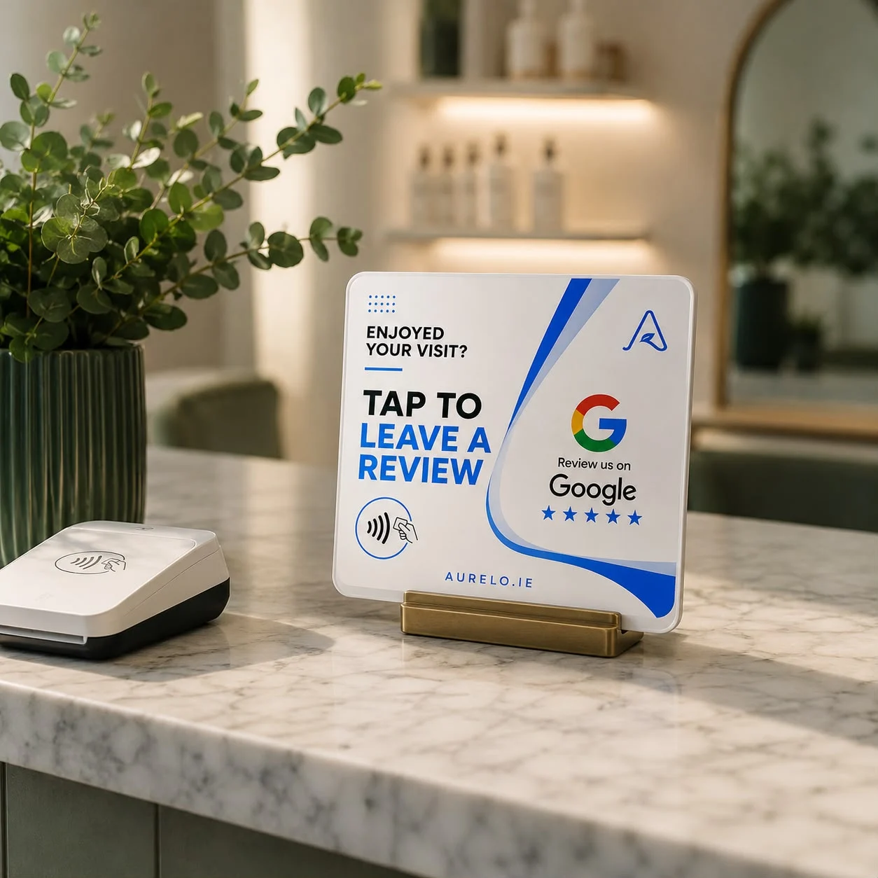 An aurelo review card standing in a brass holder on a salon reception counter, beside a card reader.